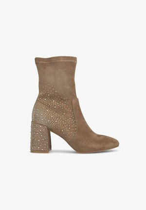 Bottine en suède beige avec bout rond, tige texturée et habillage de strass décoratifs sur le talon en bloc et le panneau latéral.