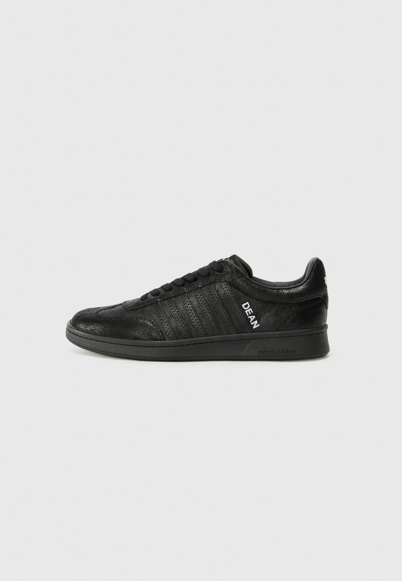 Musta tenniseking, mis on valmistatud tekstureeritud nahast, millel on lame talla, nööpidega eesosa ja külgedel valgete "DEAN" logo ribad.