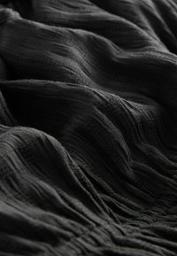 Gros plan sur un tissu sombre texturé avec des plis doux et des motifs tissés élaborés.
