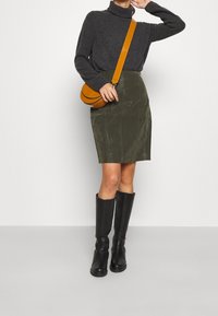 Un pull col roulé gris foncé, une jupe crayon vert olive, des bottes noires jusqu'au genou, et un sac bandoulière rond de couleur moutarde. Textures lisses et design ajusté.