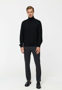 Fekete garbós pulóver hosszú ujjakkal és bordázott aljjal, sötétszürke, szabott nadrággal és fekete bőrcipővel párosítva.