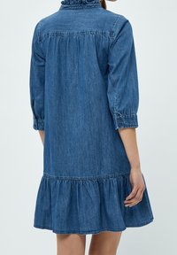 Denim dress with a ruffled collar, three-quarter sleeves, and a gathered ruffle hem. Material is soft, blue denim with subtle texture.