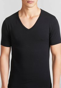T-shirt nera a maniche corte con scollatura a V, realizzata in tessuto morbido. Design aderente, aspetto semplice senza motivi visibili o dettagli metallici.