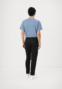 Blue cotton t-shirt with short sleeves, paired with black sweatpants featuring side stripes, and white athletic shoes.