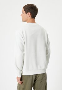 Witte sweatshirt met ronde hals, lange mouwen en geribde manchetten. Zachte textuur en een relaxte pasvorm, gecombineerd met olijfgroene cargobroek.