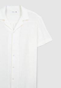 Camicia bianca a maniche corte con bottoni, realizzata in tessuto leggero. Presenta un colletto classico e cinque bottoni trasparenti sul davanti.