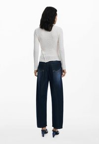 Haut blanc texturé à manches longues avec un dos fendu, associé à un jean bleu foncé à taille haute et des sandales à talons couleur marine.