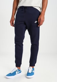 Pantalones deportivos de color azul marino hechos de un tejido suave, con una cintura elástica con cordón y un pequeño logo blanco de Nike a la altura de la rodilla.