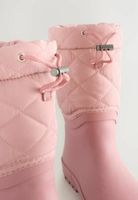Stivali impermeabili rosa con tomaia trapuntata, dotati di chiusura con cordoncino e suole in gomma. Textura liscia e design della punta rotonda.