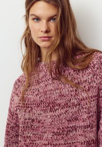 Pulover tricotat în nuanțe de roz, cu un model texturat, decolteu rotund și croială lejeră. Material moale cu variații subtile de culoare.