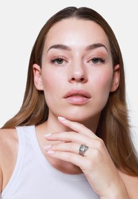 Anello in argento con design testurizzato intricato, indossato alla mano. Il modello ha capelli castani di lunghezza alla spalla, pelle chiara e smalto neutro sulle unghie.