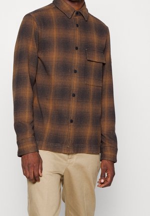 Brown and black checkered shirt in a textured fabric with a collar and button closure. Features a chest pocket and long sleeves.