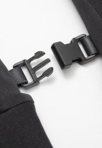 Juodas plastikinis sagtis, plokščias ant tekstūruoto juodo diržo, su reguliuojamu užsegimu. Sagtis turi spyruokles, skirtas tvirtinimui ir uždarymui.