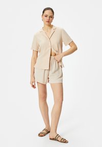 Lichtbeige overhemd met korte mouwen en knoopjes, in een ontspannen pasvorm, gecombineerd met bijpassende shorts; beide zijn gemaakt van een zachte, gestructureerde stof.