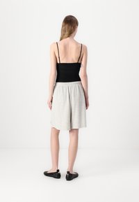 Černý přiléhavý top na ramínka, světle šedé šortky střední délky s elastickým pasem a černé nazouvací boty. Hladká tkanina, jednoduchý design.