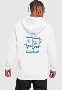Hvid hættetrøje med et tegneseriedesign af to kaffekopper med ansigtstræk, teksten "mere espresso mindre depressi" og en taleboble.