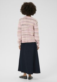 Adīts džemperis pasteļa rozā krāsā ar daudzkrāsainām svītrām, apvienots ar garu tumšo džinsu svārku un melniem apaviem ar spidolu.