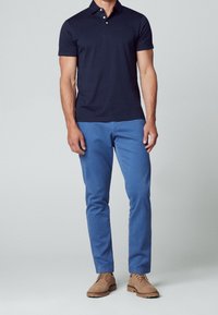 Polo bleu marine à manches courtes, patte de boutonnage à deux boutons ; associé à un chino bleu et des chaussures lacées marron clair. Texture de coton lisse.