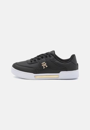 Czarny niski sneaker z białą podeszwą, złotym akcentem na śródpodeszwie, sznurowanym zapięciem oraz złotym logo "TH" na bocznym panelu.