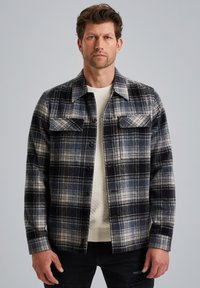 Ruudullinen takki tummansinisessä, mustassa ja valkoisessa värissä. Oma avokauko, nappikiinnitys ja kaksi rintataskua. Päällä teksturoitu valkoinen villapaita.