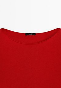 Col en rond d'un pull rouge avec une petite étiquette noire indiquant « Massimo Dutti Made in China » centrée à l'intérieur du col.