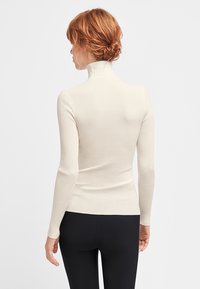 Ribbet, cremefarvet turtleneck sweater med lange ærmer, tætsiddende silhuet og blød tekstur. Båret med sorte tights.