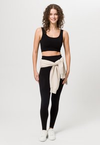 Černý crop top a legíny doplněné béžovou mikinou uvázanou v pase. Bílé tenisky dokončují outfit. Jednoduchý, přiléhavý design.