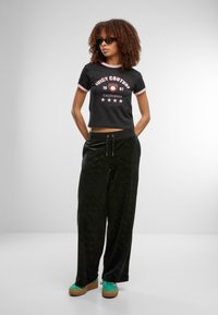 Černé zkrácené tričko s růžovým lemováním a logem Juicy Couture; černé sametové kalhoty s širokými nohavicemi a jemným vzorem; zelené platformové tenisky.