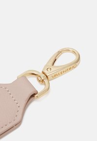 Gaiši rozā siksniņa ar teksturētu virsmu un zelta tonēts metāla klips. Klipsā ir ierakstīts vārds "VALENTINO." Vienkāršs, funkcionāls dizains.