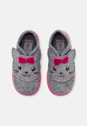 Zapatillas grises para niños con caras de gato brillantes, mejillas rosadas, bigotes negros y lazos de terciopelo rosa en la parte superior, con la etiqueta Superfit en el interior.
