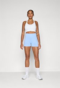 Un soutien-gorge de sport blanc et un short taille haute bleu clair, fabriqués en tissu lisse, associés à des baskets blanches et des bas jusqu'aux genoux.