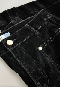 Černé džíny z denimu s měkkou texturou, s akcenty z mosazných knoflíků, bílým prošitím a modrou štítkovou na pásku.