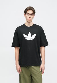 Czarny bawełniany t-shirt z dużym białym logo Adidas w kształcie koniczyny z przodu. Krótkie rękawy, okrągły dekolt i luźny krój.