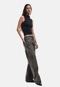 Top negro ajustado sin mangas combinado con pantalones sueltos de estampado de leopardo. Los pantalones tienen una cintura natural y un diseño de pierna acampanada.