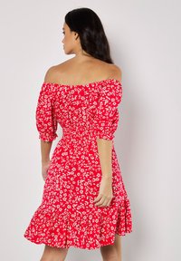 Rotes florales Off-Shoulder-Kleid mit Puffärmeln, gerafft im Oberteil und mit Rüsche am Saum. Hat weiße blumige Muster und einen leichten Stoff.