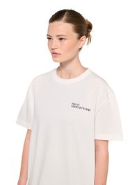 Junge Frau mit Dutt trägt ein weißes T-Shirt mit "HALO 196819721981" auf der linken Brust und blickt nach rechts.