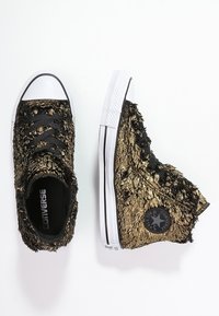 Vysoké tenisky Converse s černou a zlatou kožešinovou strukturou, bílé gumové podešve a černé tkaničky. Na boku nášivka se symbolem hvězdy.