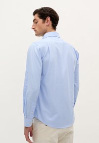 Camicia azzurro chiaro a maniche lunghe con colletto button-down, caratterizzata da un sottile motivo a quadretti e polsini con un solo bottone, realizzata in tessuto intrecciato.