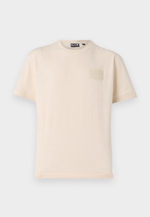 T-shirt à manches courtes de couleur crème en coton, avec un patch logo texturé de la marque sur la poitrine gauche et un col rond classique.