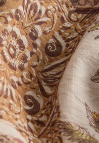 Tissu marron et beige avec des motifs floraux et de feuilles complexes, montrant une texture détaillée et des plis.