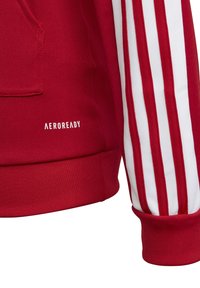 Rød sweatshirt med tekstureret stof, hvide vandrette striber på ærmerne, kengurulomme og "AEROREADY" logo i hvid.