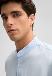 Lichtblauw, collared shirt met een soepele structuur, met knoopsluiting aan de voorkant en een slim fit ontwerp. Zichtbare glans van de stof en fijne stikseldetails.