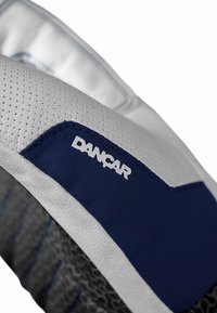 Zapatilla blanca con una superficie texturizada, acentos en azul marino y un logo. Presenta una suela de goma con diseño y material transpirable.