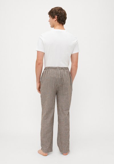 Heren pyjamabroek in bruin en wit geruit met een elastische tailleband, rechte pijpen en lichte stof. Draagt met een plain witte T-shirt.