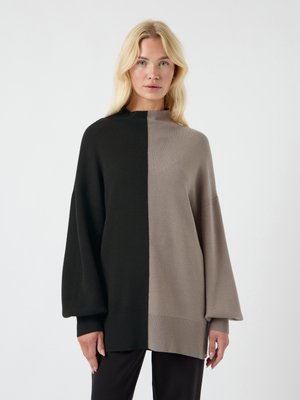 Overdimensjonert genser med delt design i svart og lysebrune farger, med brede ermer og ribbestrikkede detaljer på nederkant og mansjetter.