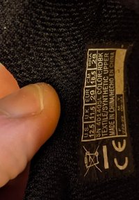 Etichetta in tessuto nera che mostra informazioni su taglia e cura. Comprende taglie USA, UK ed EU, paese di origine e simbolo di non lavaggio.