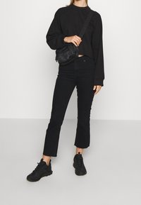 Black cropped sweatshirt, black high-waisted jeans with frayed hem, and black athletic shoes. Adjustable strap bag worn crossbody.