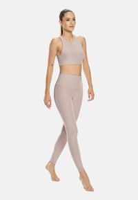 Svetlo roza športni komplet, ki vključuje skrajšan top s gladko površino in hlače z visokim pasom ter teksturiranim pasom.