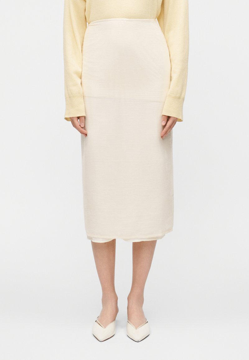 Kremasta suknja dužine do koljena s teksturiranim tkanjem. Ima srednje visok pojas, ravni kroj i suptilne detalje na rubu.