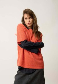 Suéter de mezcla de lana naranja con mangas cortas, usado sobre una camisa negra de cuello. La textura parece suave; el dobladillo es recto y relajado.